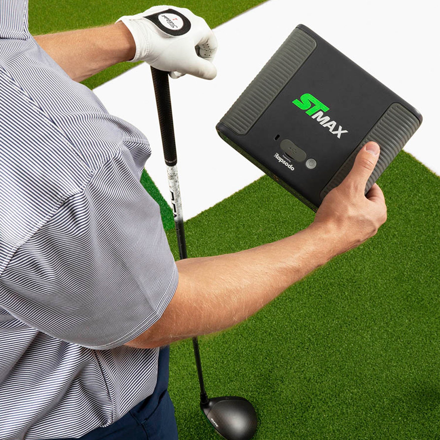 Golfer holding SKYTRAK ST MAX launch monitor on premium hitting mat with driver for indoor golf practice